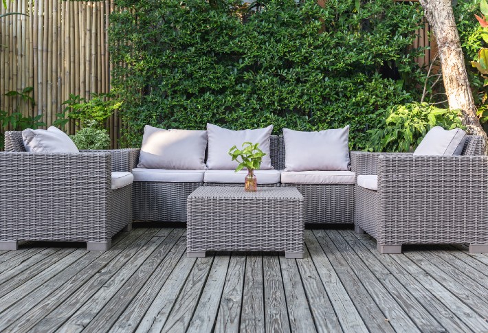 A grey patio conversation set on a wooden deck, framed by a green hedge, showcasing one of the best patio conversation sets.